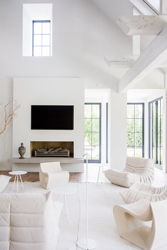 Sofás y sillones en blanco, chimenea, paredes con vigas de madera en blanco, perfilería de ventanas en negro