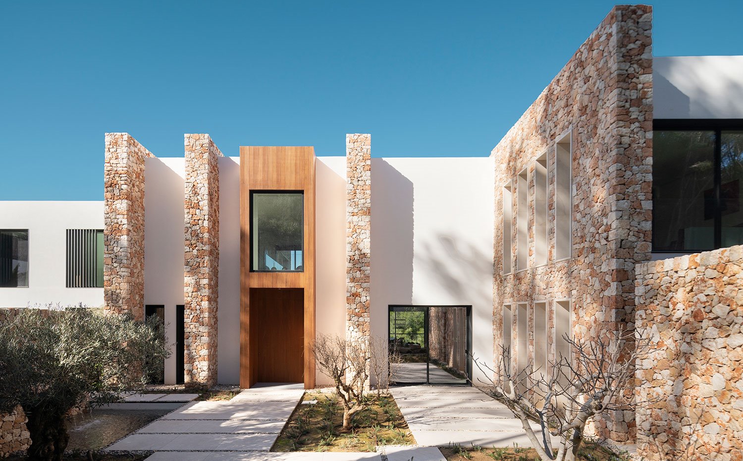 Entrada principal de la casa con estructura central revestida de madera y muros de piedra