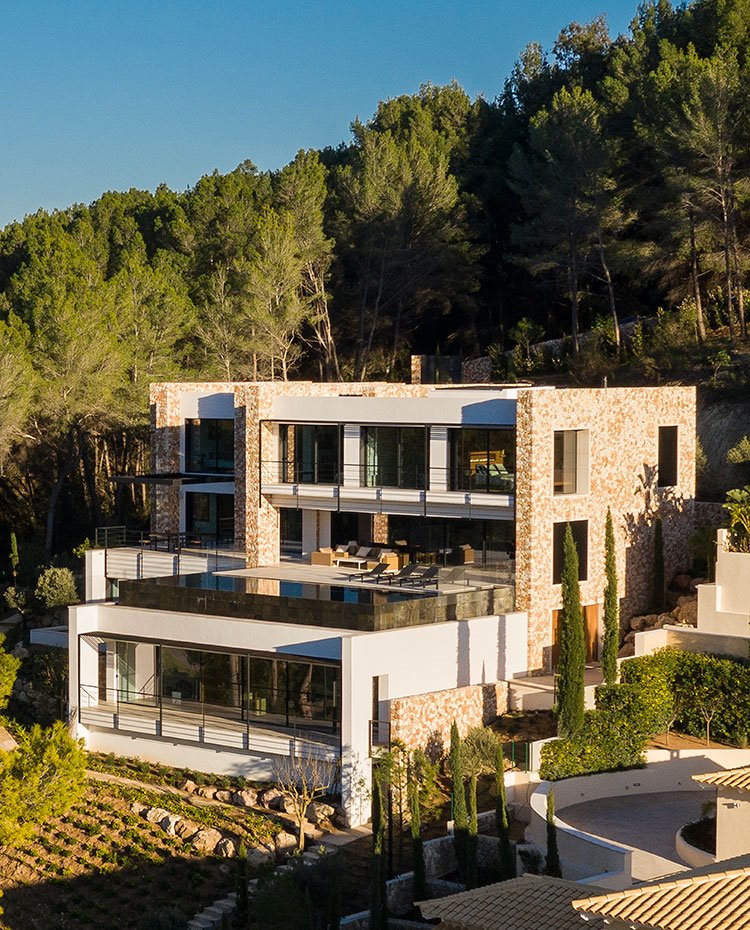 Exterior de la vivienda con fachada en blanco y piedra, rodeada de una densa vegetación