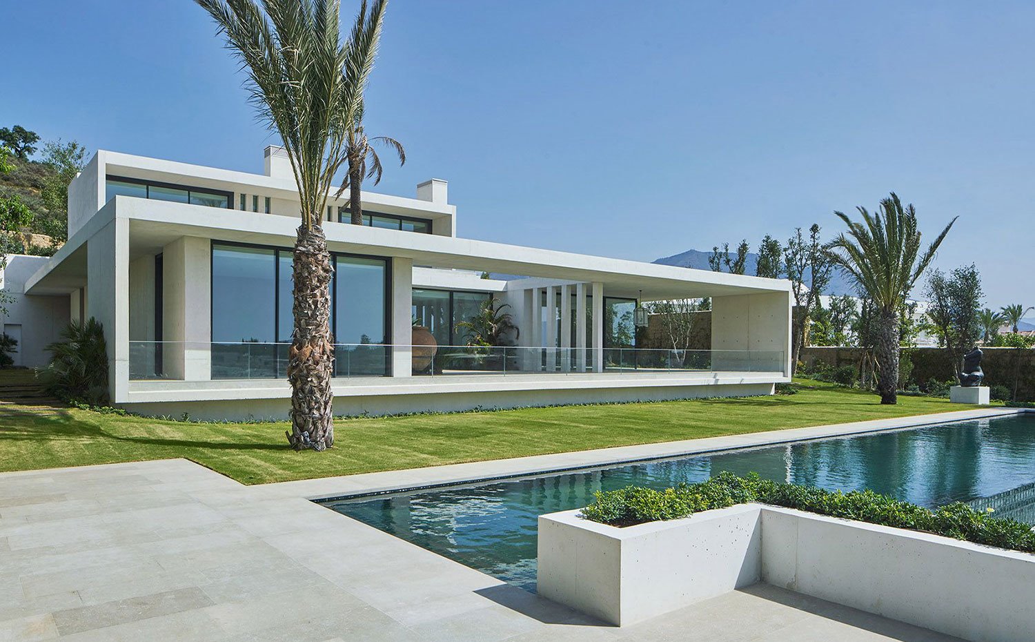 Porche y terraza que asoman a jardín con palmeras y piscina