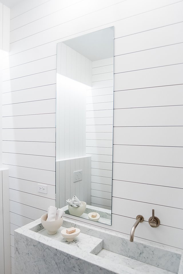 Lavamanos de marmol con paredes de madera blanca y espejo