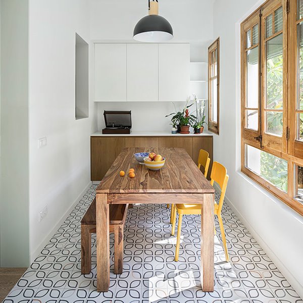 Comedor con mesa y banco de madera y sillas en amarillo, luminaria de suspensión con patalla en negro y detalles dorados, mueble almacenaje en pared en blanco y madera