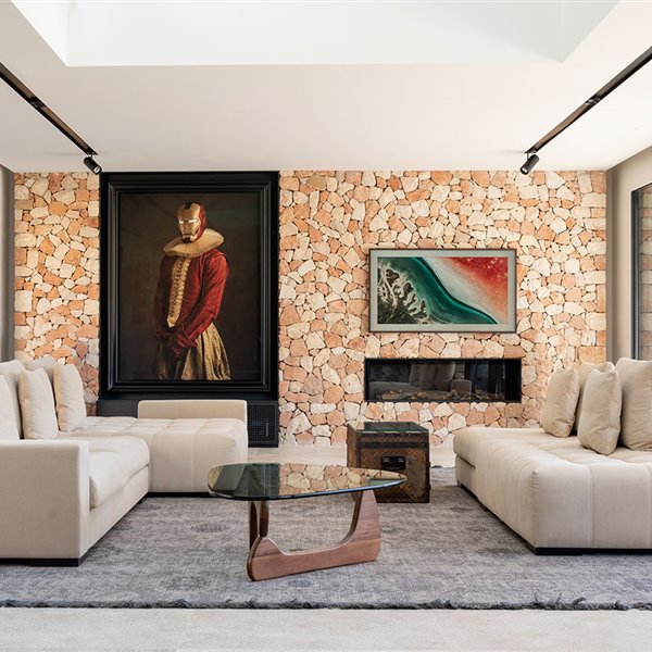 Salón con grandes sofás en tonos crudo, mesa de centro de cristal y madra, alfombra gris y pared revestida de piedra con chimenea integrada