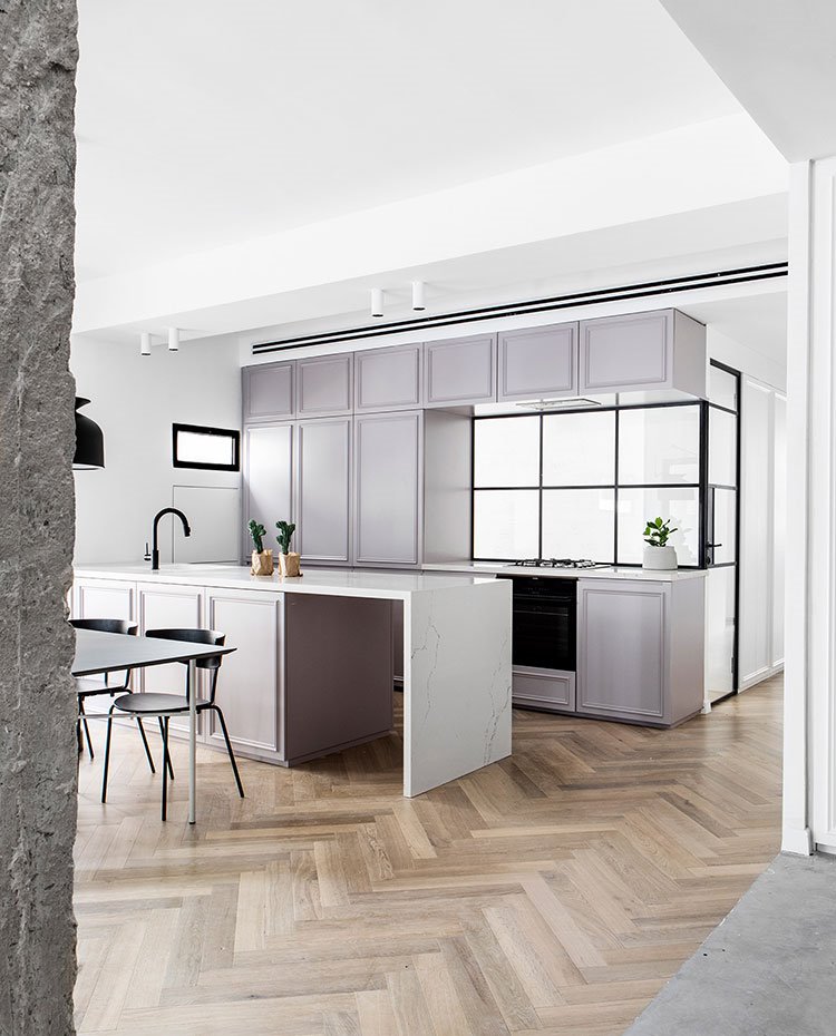 Cocina abierta con isla de trabajo con encimera blanca y mesa de comedor. 