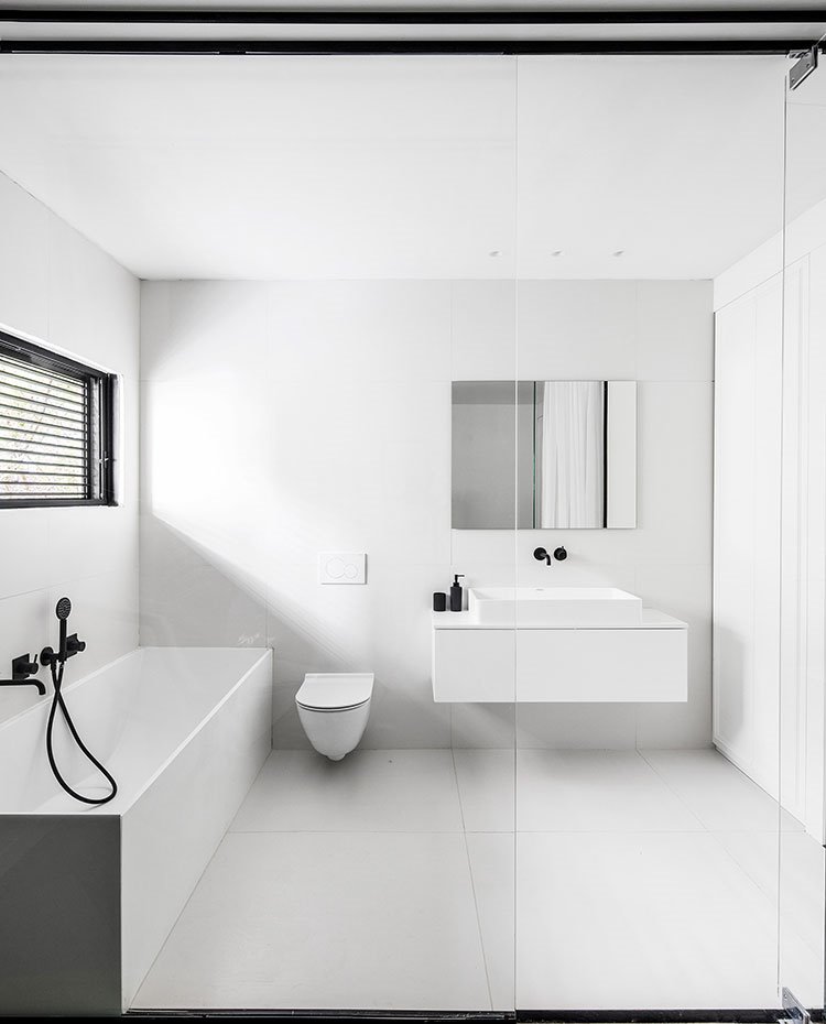 Cuarto de baño con gresite gris claro en suelo y revestimiento, mueble bajo lavamanos blanco y grifería en negro