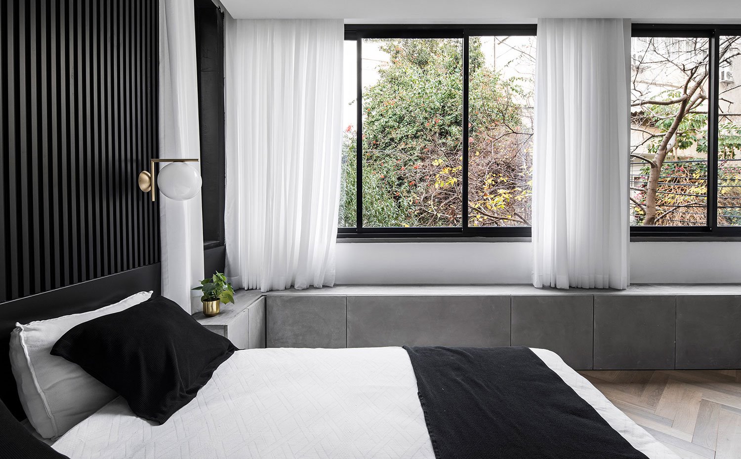 Dormitorio principal con cabecero negro en listones, grandes ventanales a exterior y módulos bajos en gris a lo largo de todo el perímetro