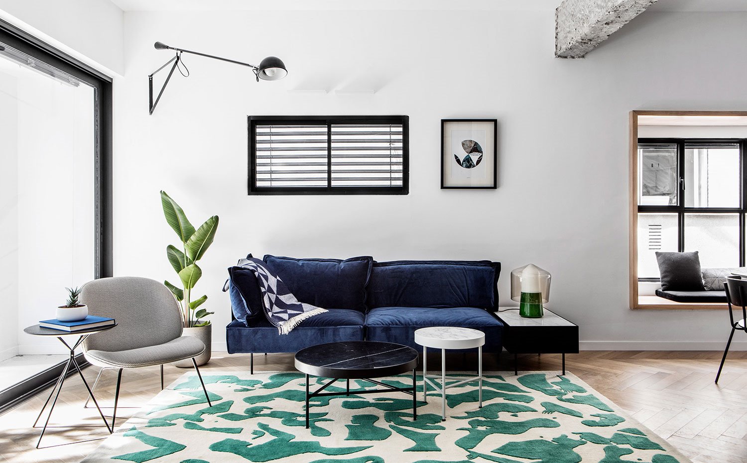 Salón con sofá aterciopelado azul, butaca gris y alfombra blanca y verde