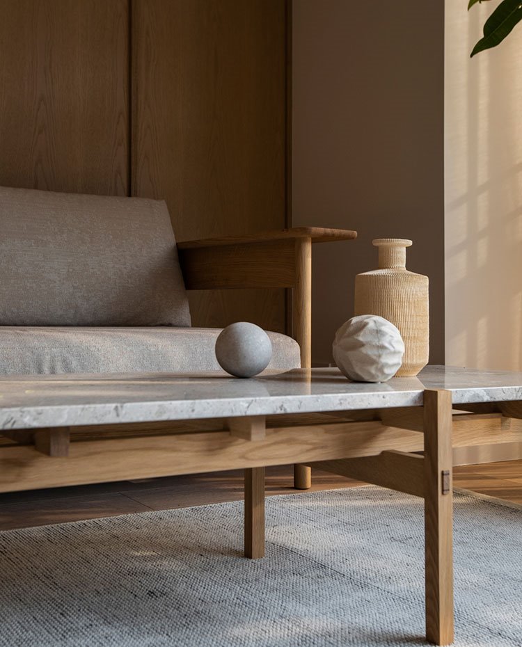 Detalle mesa de centro con sobre de piedra gris y estructura de madera, detalles decorativos en piedra
