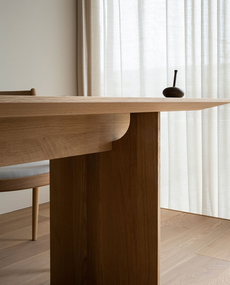 Detalle mesa en madera, cortinas cridas ante cerramientos de cristal