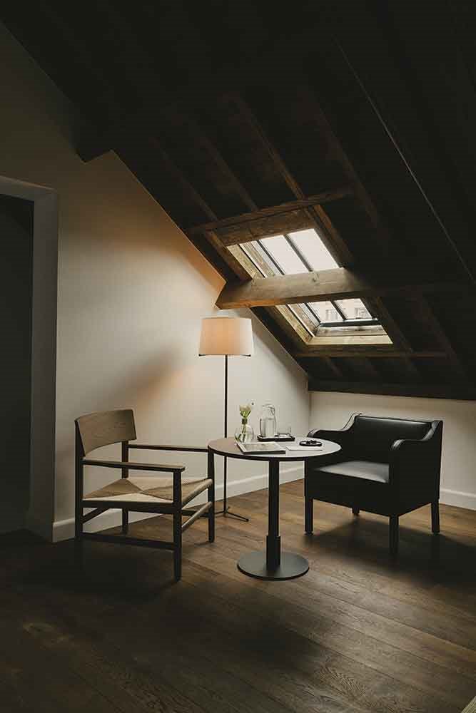 HAbitacion-buhardilla-con-sillas-mesas-y-lampara-en-el-hotel-August-de-Amberes-con-la-reforma-de-Vincent-van-Duysen