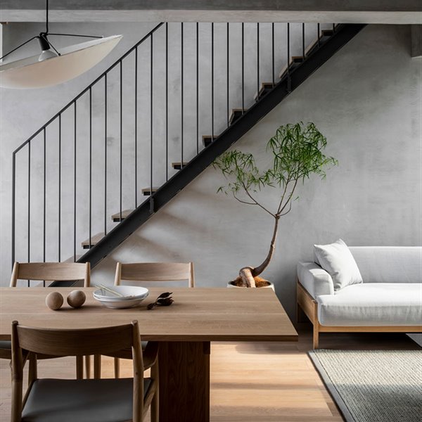 Mesa y sillas de madera, luminaria suspendida con pantalla semicircular, escaleras de madera y acero, sofá en gris