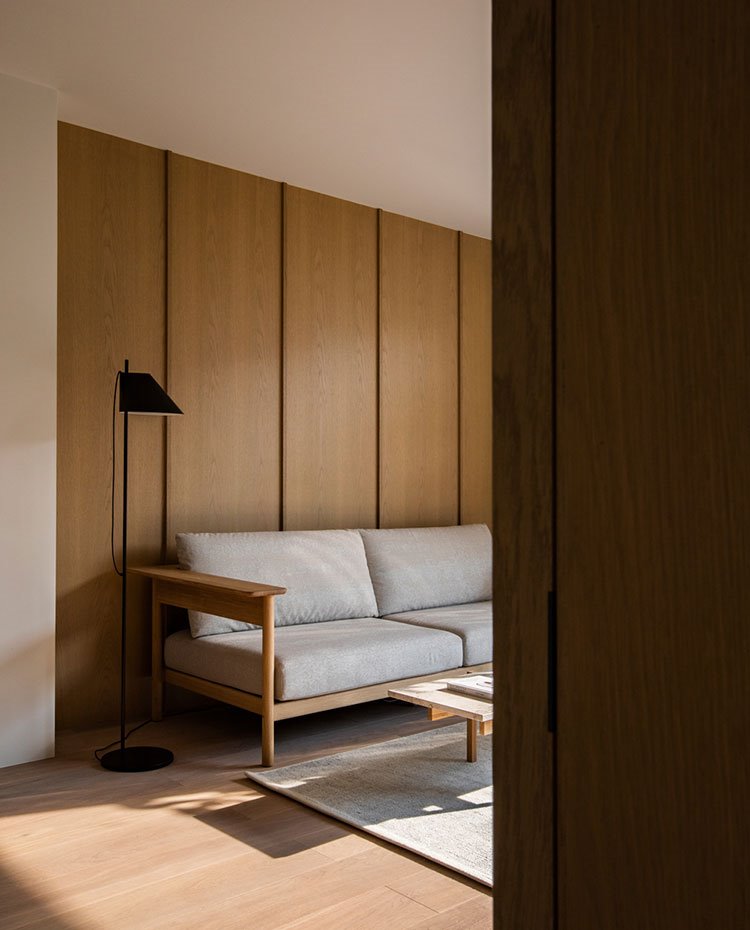 Revestimiento de pared de madera, sofá en gris, luminaria de pie negra