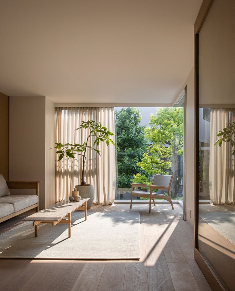 Sala con suelo de madera, alfombra cruda, sofá y butaca en madera y tapicería en crudo