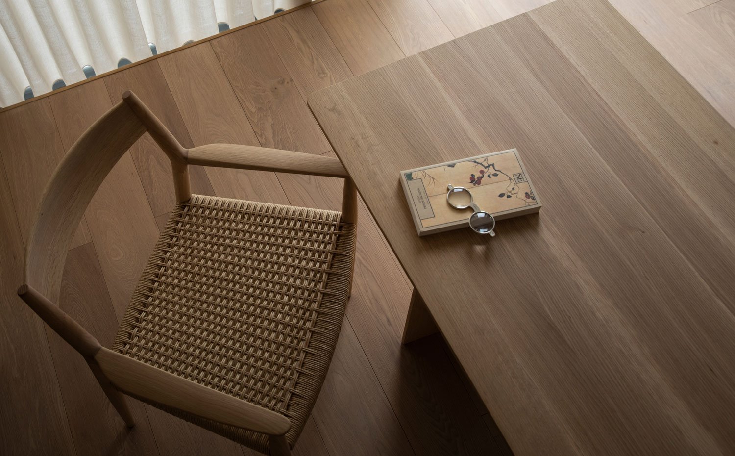 Silla, mesa y pavimento de madera, libro y anteojos sobre mesa