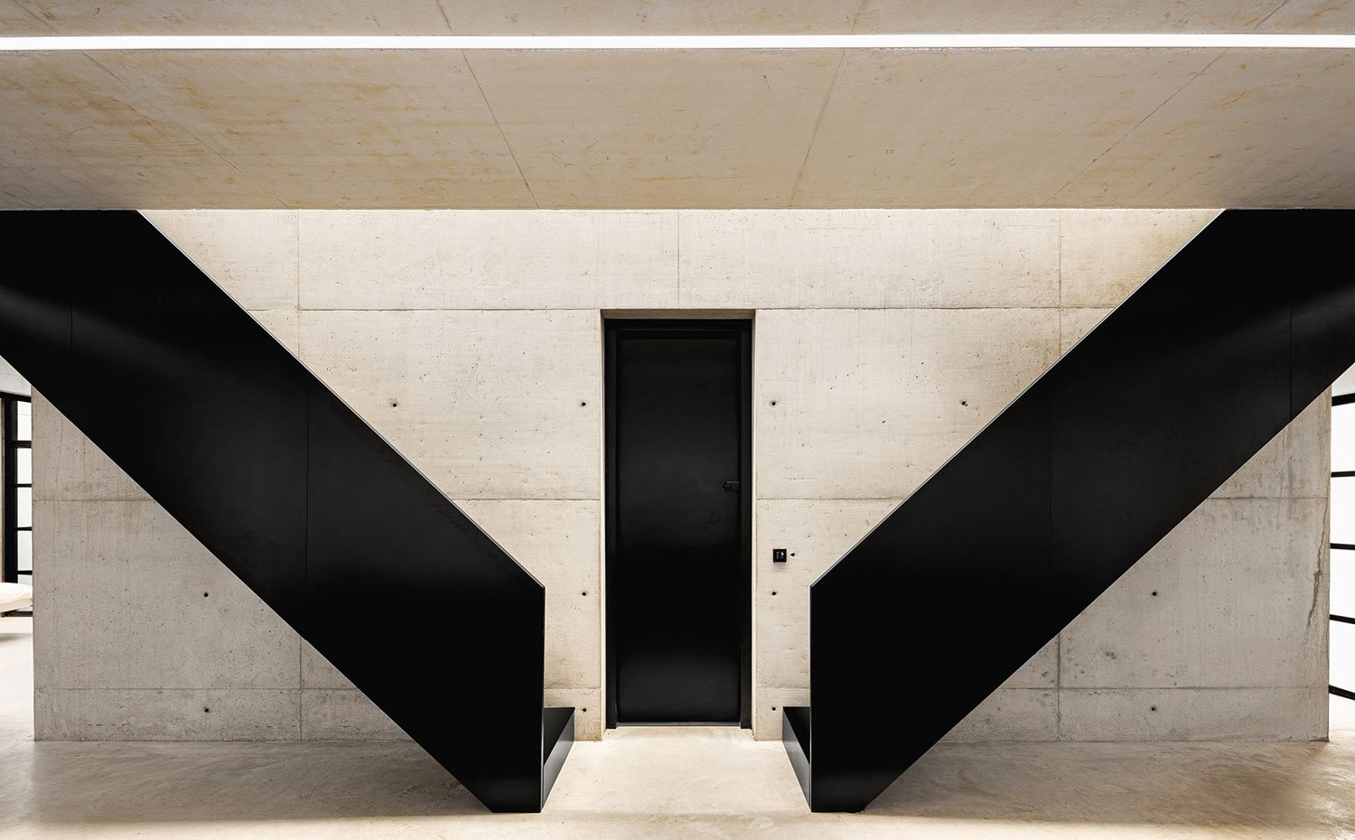 Estructura de escaleras en negro, en V, puerta lacada negra con revestimiento y suelo de hormigón