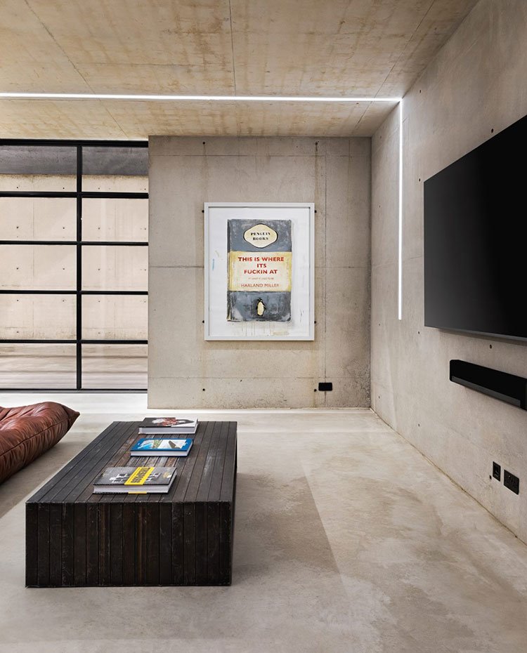 Salón con mesa de centro de madera y televisor y altavoz colgados de la pared. Todo el revestimiento de hormigón