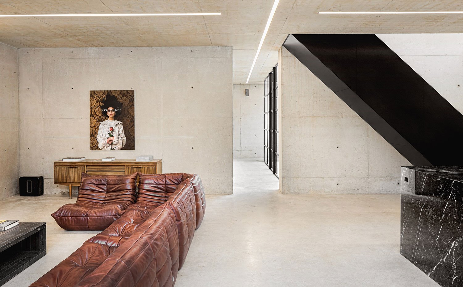 Salón sofá de piel marron, revestimiento de hormigón, escaleras con caja negra 