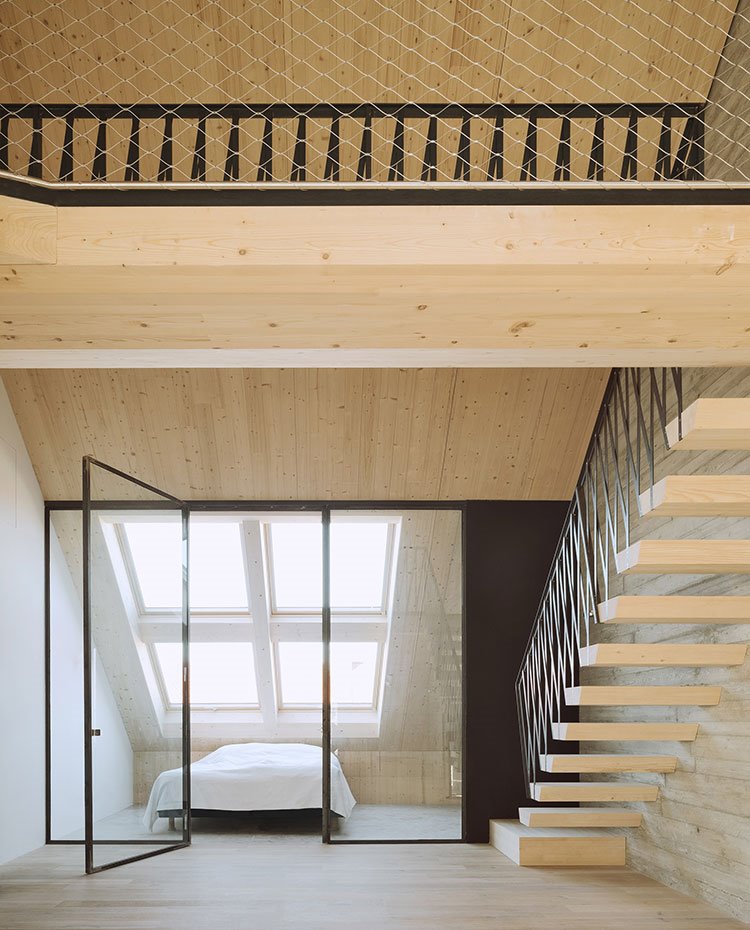 Dormitorio con cerramiento de cristal y grandes ventanales en la cubierta, con escalera a base de peldaños de madera y estructura cromada