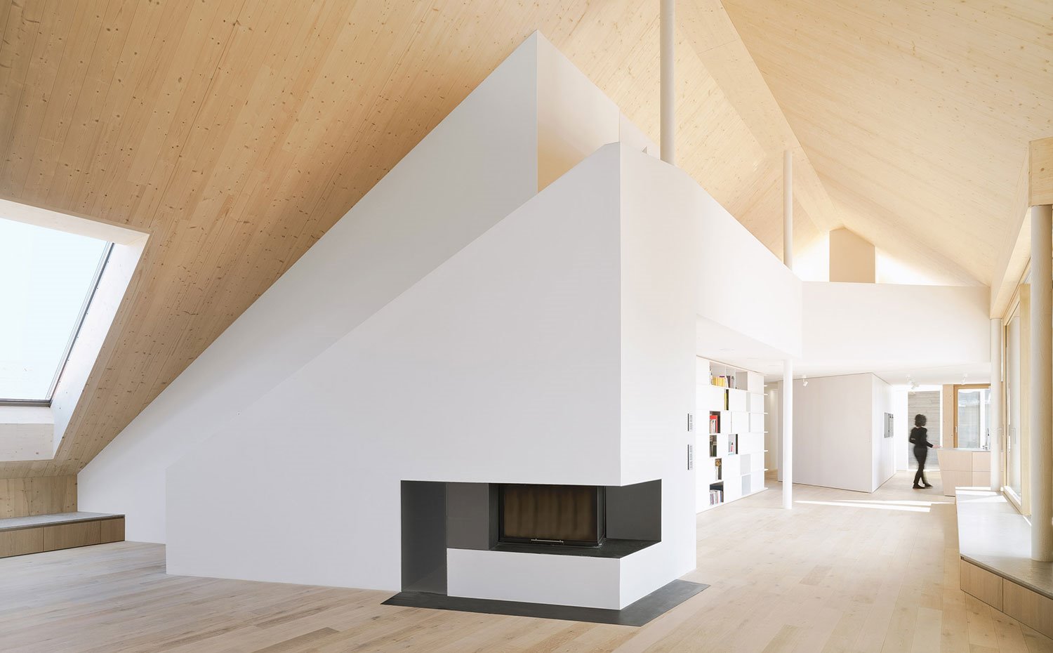 Salón con chimenea, estantería bajo hueco pasarela nivel superior y cocina al fondo