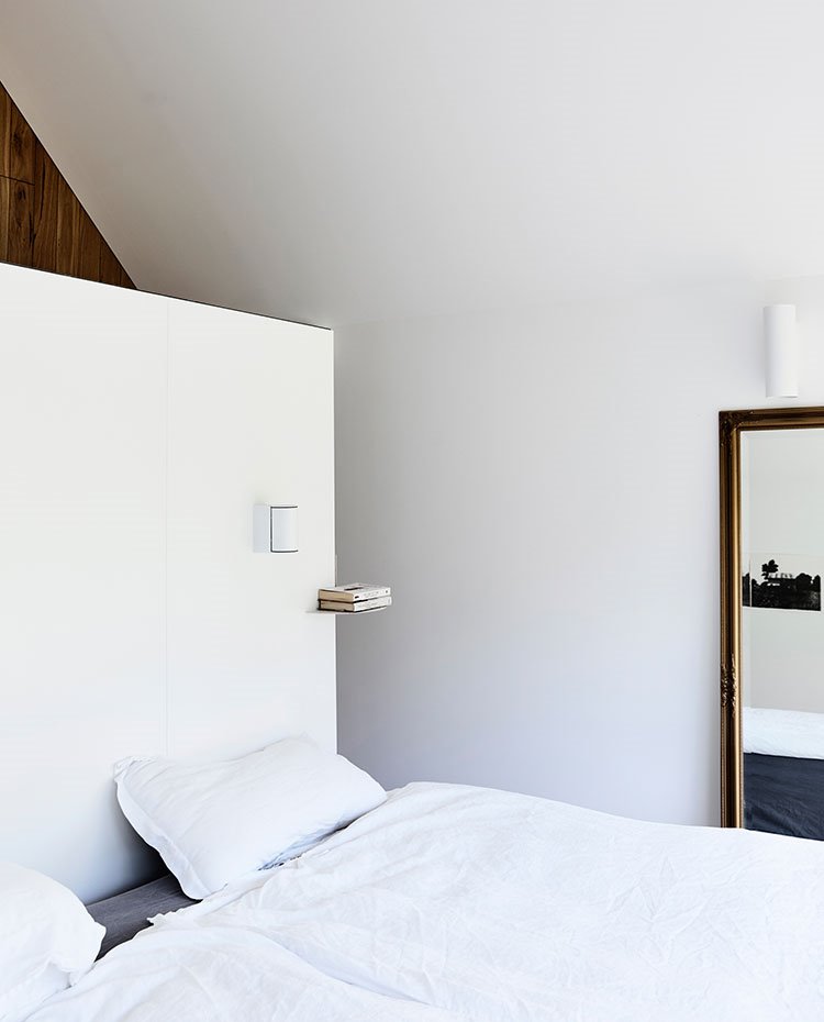 Dormitorio-con-murete-blanco-en-cabezal,-espejo-lateral-y-repisa-para-libro