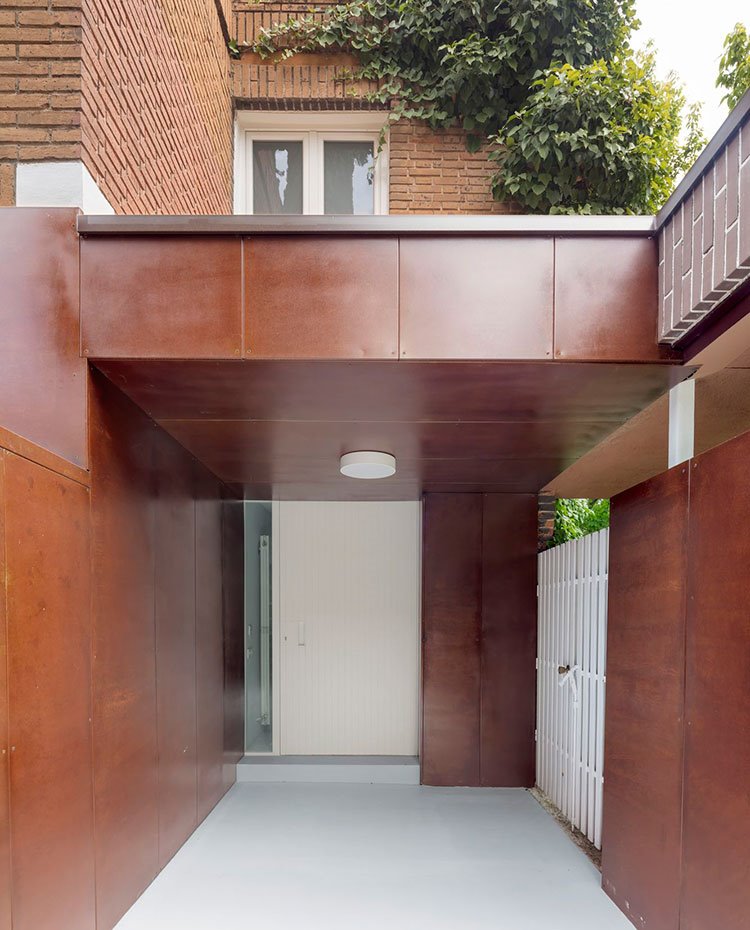 Entrada-vivienda,-revestimiento-en-madera,-ladrillo-visto,-suelo-en-gris-y-cerramientos-en-blanco