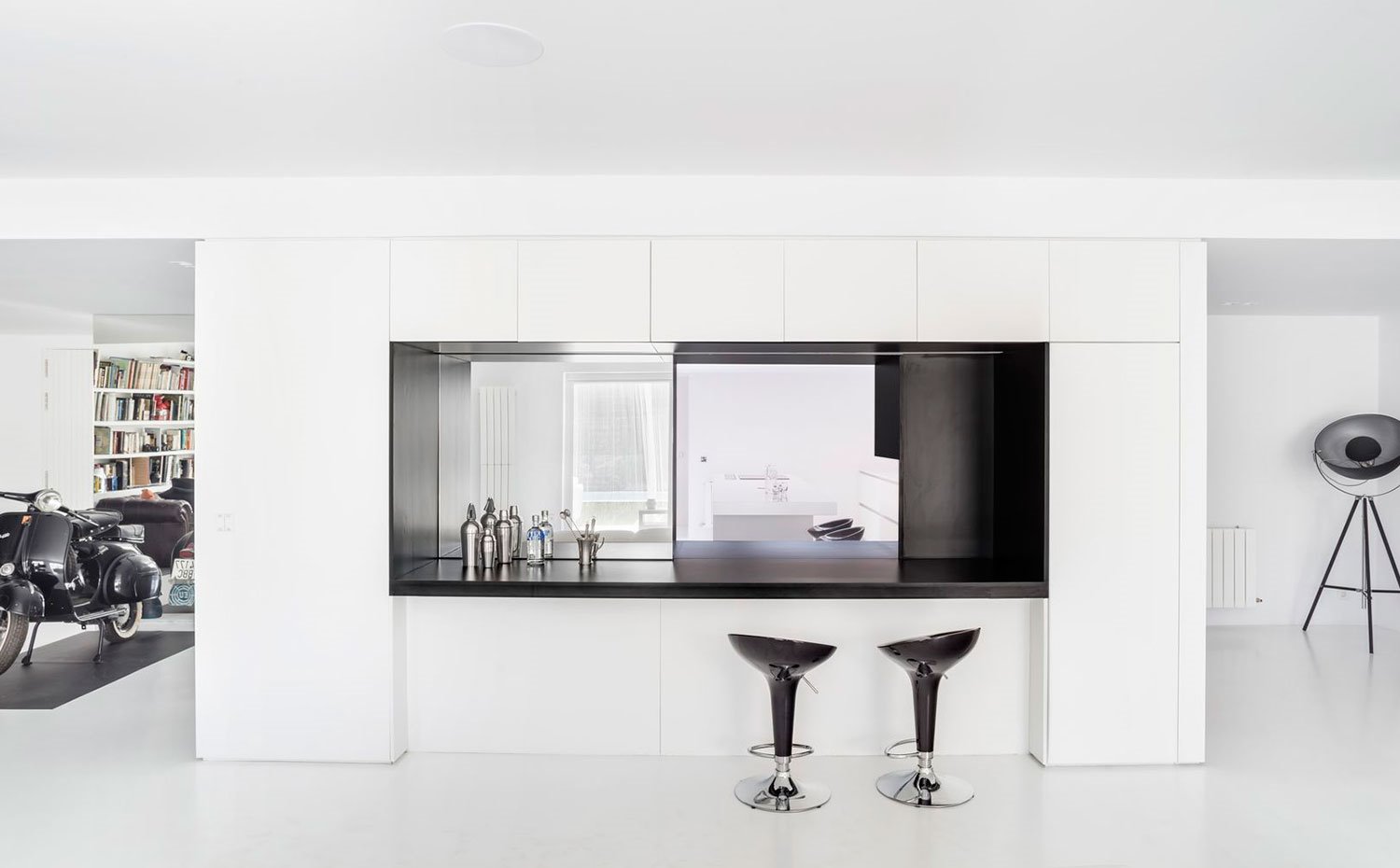 Módulo-divisor-con-zona-para-office-y-barra-para-mini-bar,-apertura-hacia-cocina,-moto-negra,-lámpara-de-pie-a-modo-de-foco