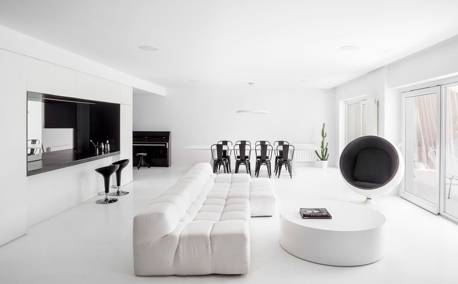 Salón-con-sofá-blanco,-mesa-centro-circular-blanca,-ball-chair,-sillas-comedor-metálicas-negras,-mesa-de-centro-blanca-rectangular,-taburetes-office-negro