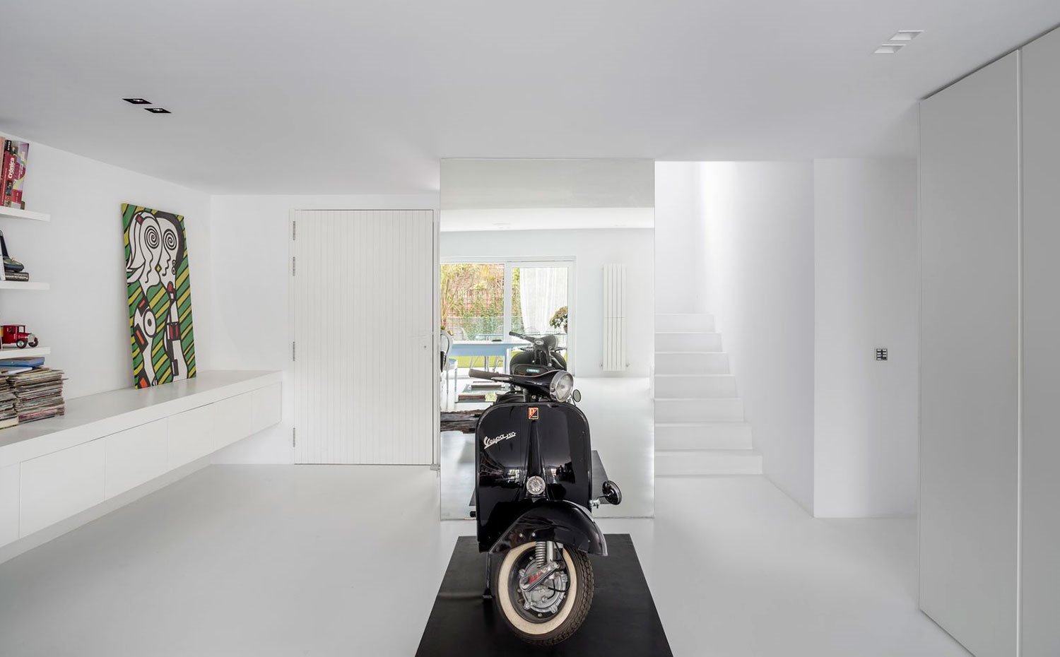 Zona-de-acceso-con-moto-negra,-mueble-bajo-suspendido-en-blanco-en-todo-ancho-de-pared,-escaleras-a-piso-superior