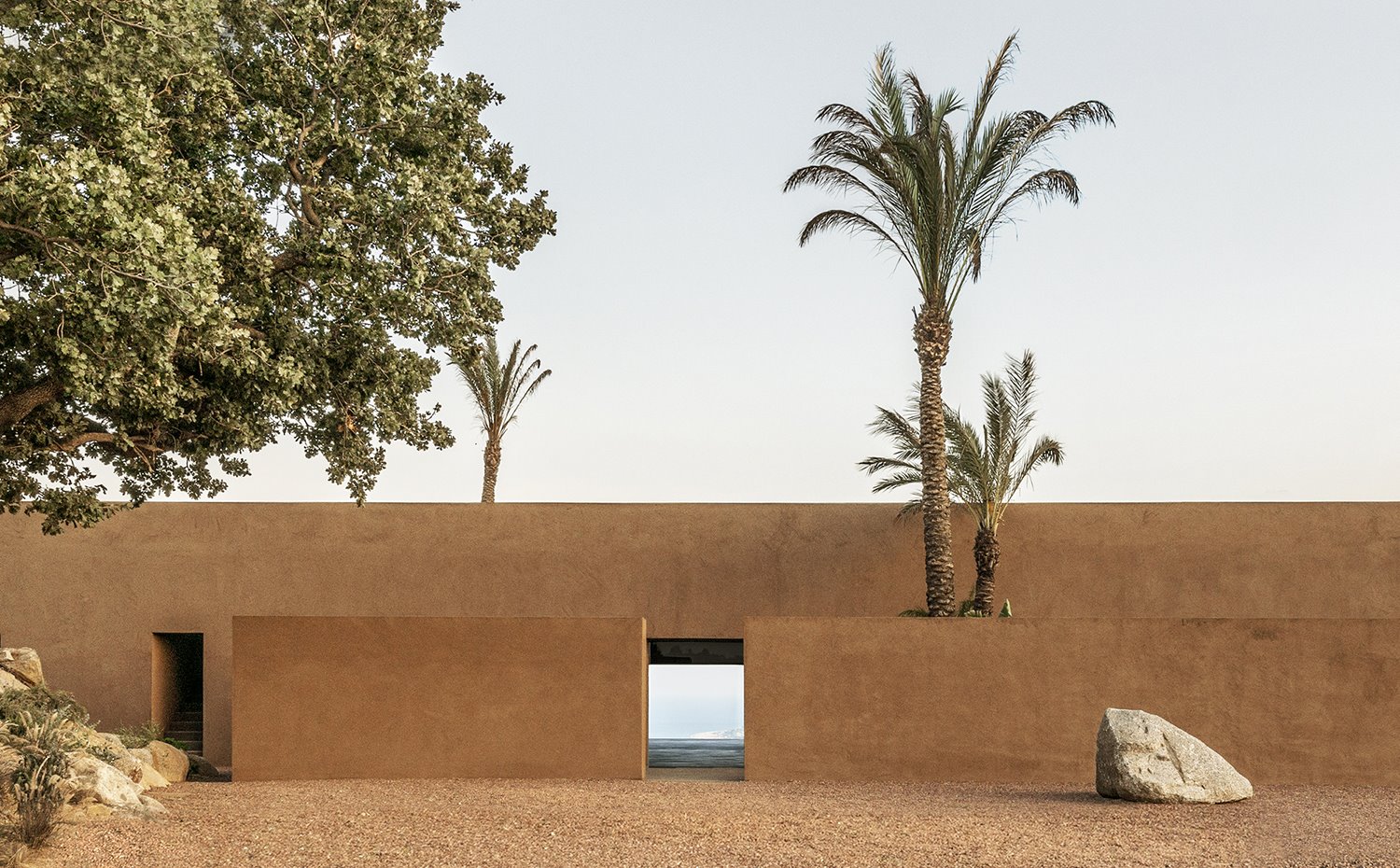 Exterior de tierra con estructura vivienda terrosa con grandes rocas y palmeras