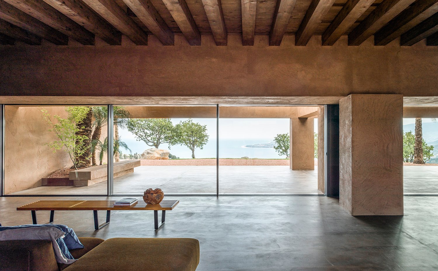 Interior salón con sofá de tonos tierra, mesa de centro con sobre de madera y aperturas de cristal