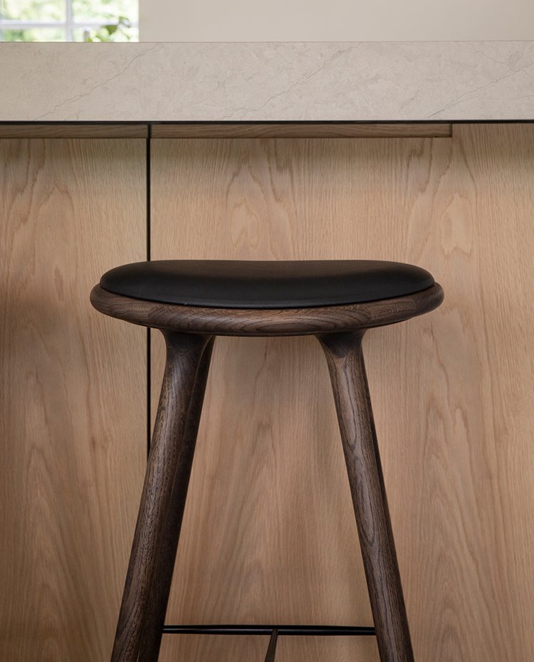 Taburete en madera oscura y asiento negro junto a mobiliario con tirador integrado y encimera de piedra