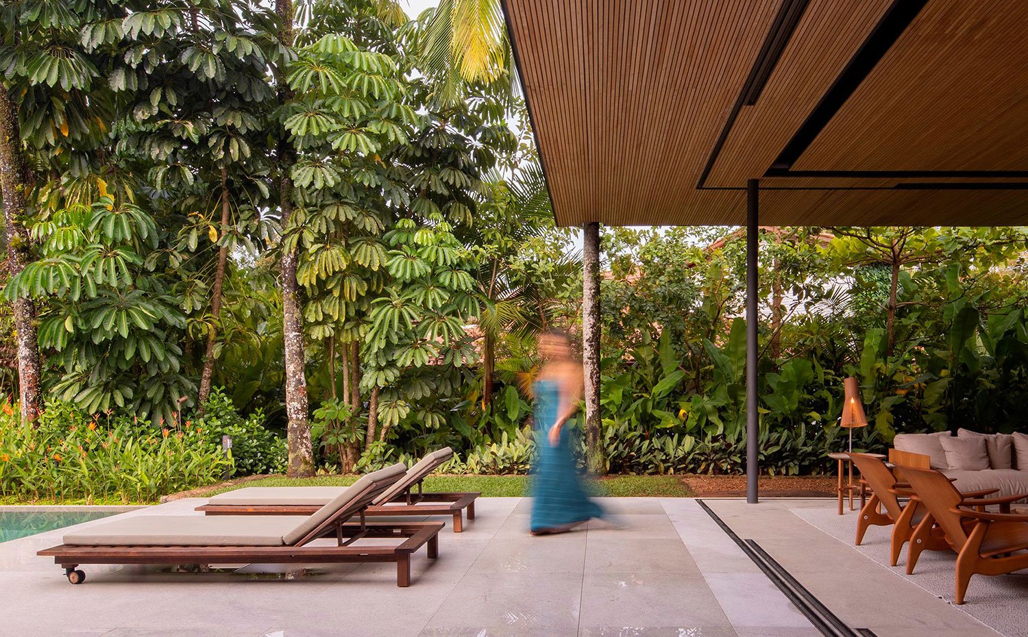 Salón abierto al exterior, cubierta de madera alistonada y tumbonas marrones junto a la piscina