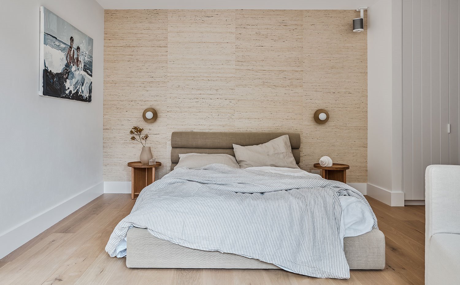 Cama con ropa de cama a raya, mesillas de noche de madera, frente de pared revestido de tonos beiges