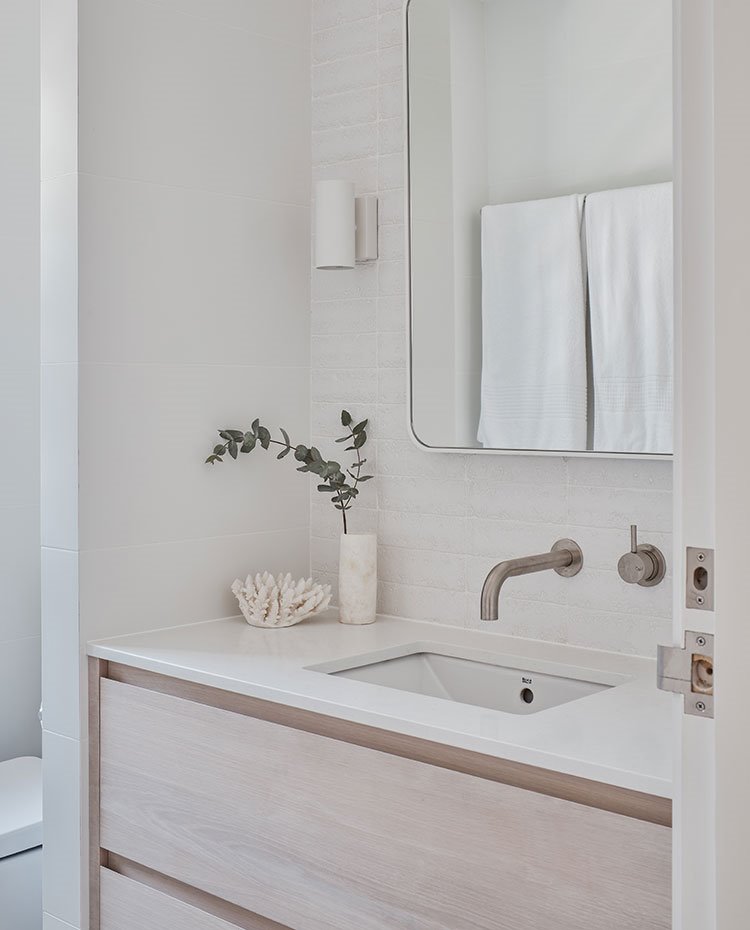 Cuarto de baño con encimera de silestone blanco, mueble madera clara, revestimiento porcelánico 