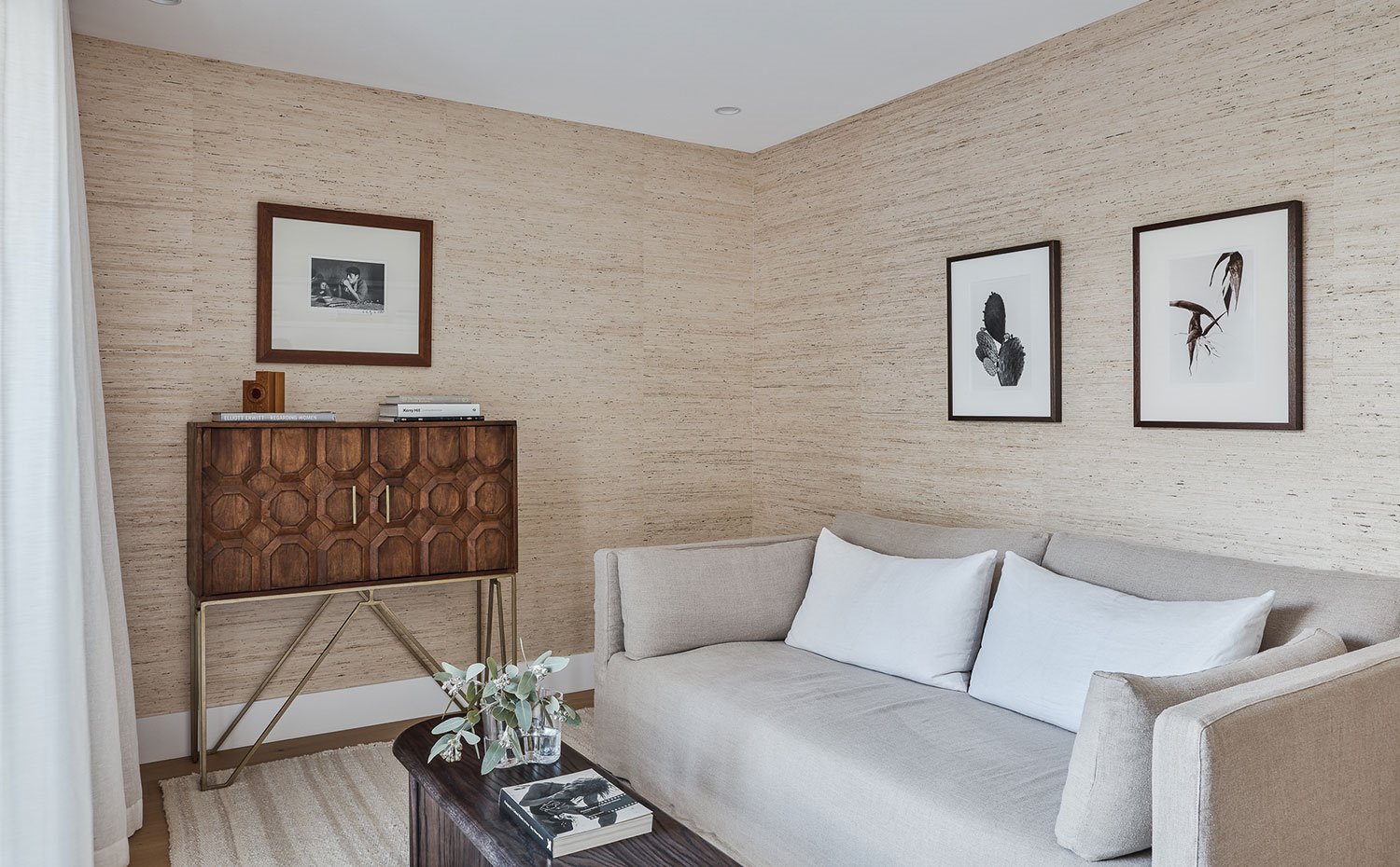 Zona de estar con mesa alargada de madera, sofá beige con cojines crudos y aparador de madera y patas cromadas 
