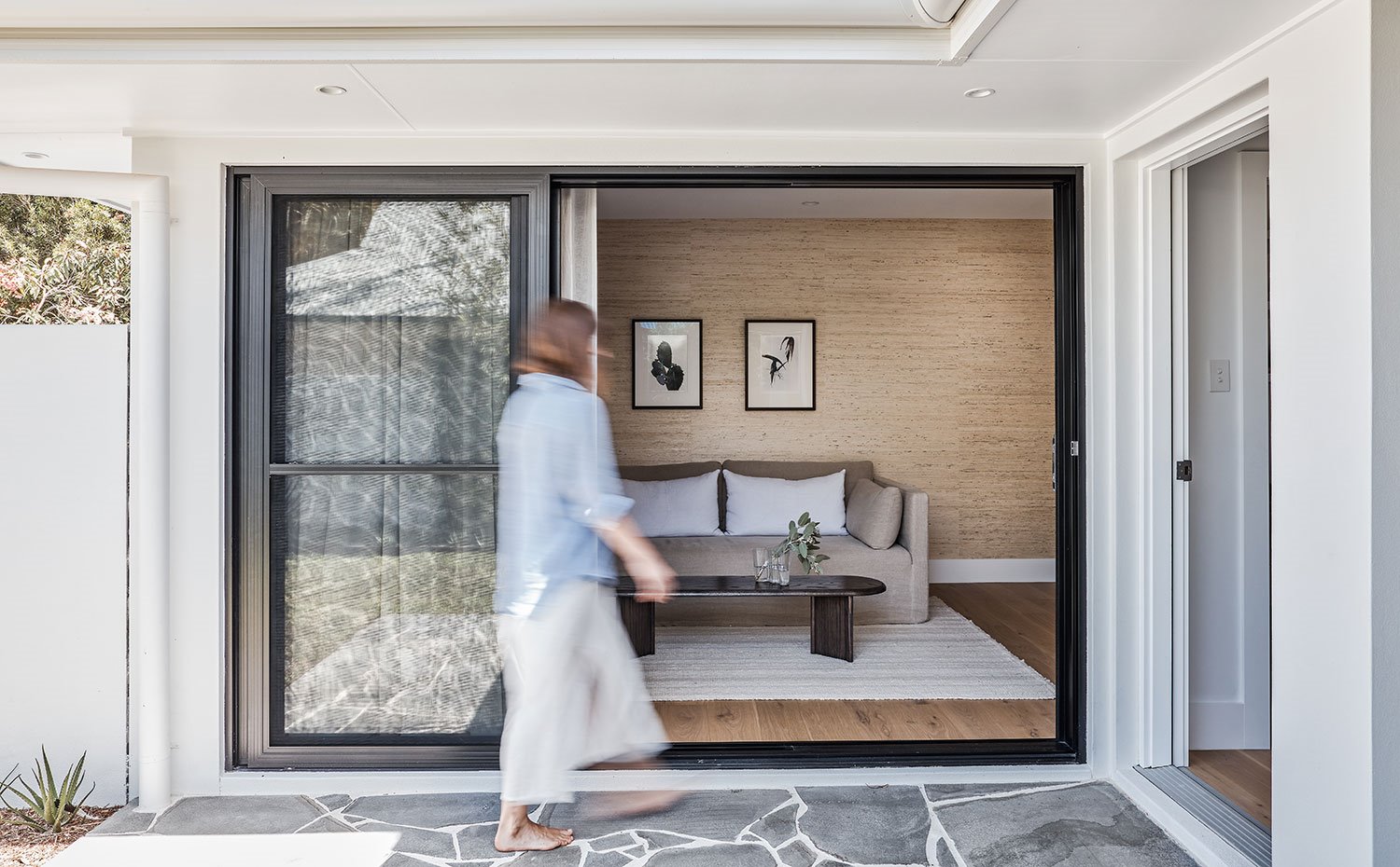 Zona exterior con suelo de pizarra, cerramiento corredero frente a sofá y mesa de madera oscura