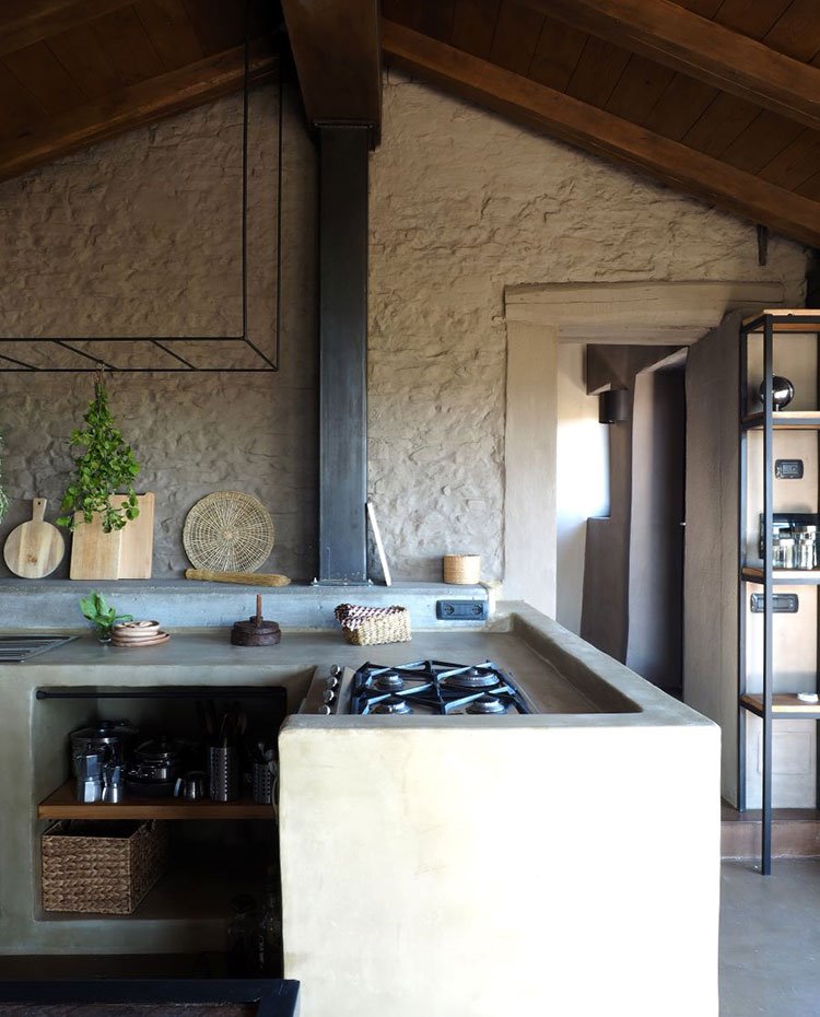 Cocina de obra con huecos en compartimientos inferiores, techo a dos aguas y estanterías de hierro y madera