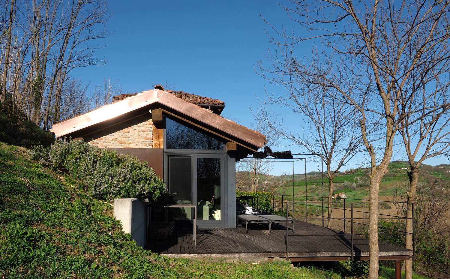 Exterior de vivienda de piedra vista, madera, hierro y cristal con porche y terraza