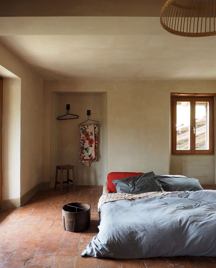 Habitación con hueco para colgadores, taburete de madera, lámpara de techo de fibras, cama sobre suelo de gres