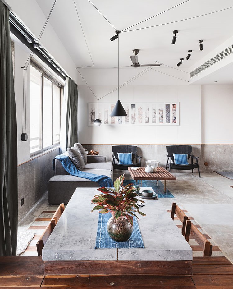 Mesa de comedor con sobre de piedra gris con sillas de madera, al fondo la zona de salón