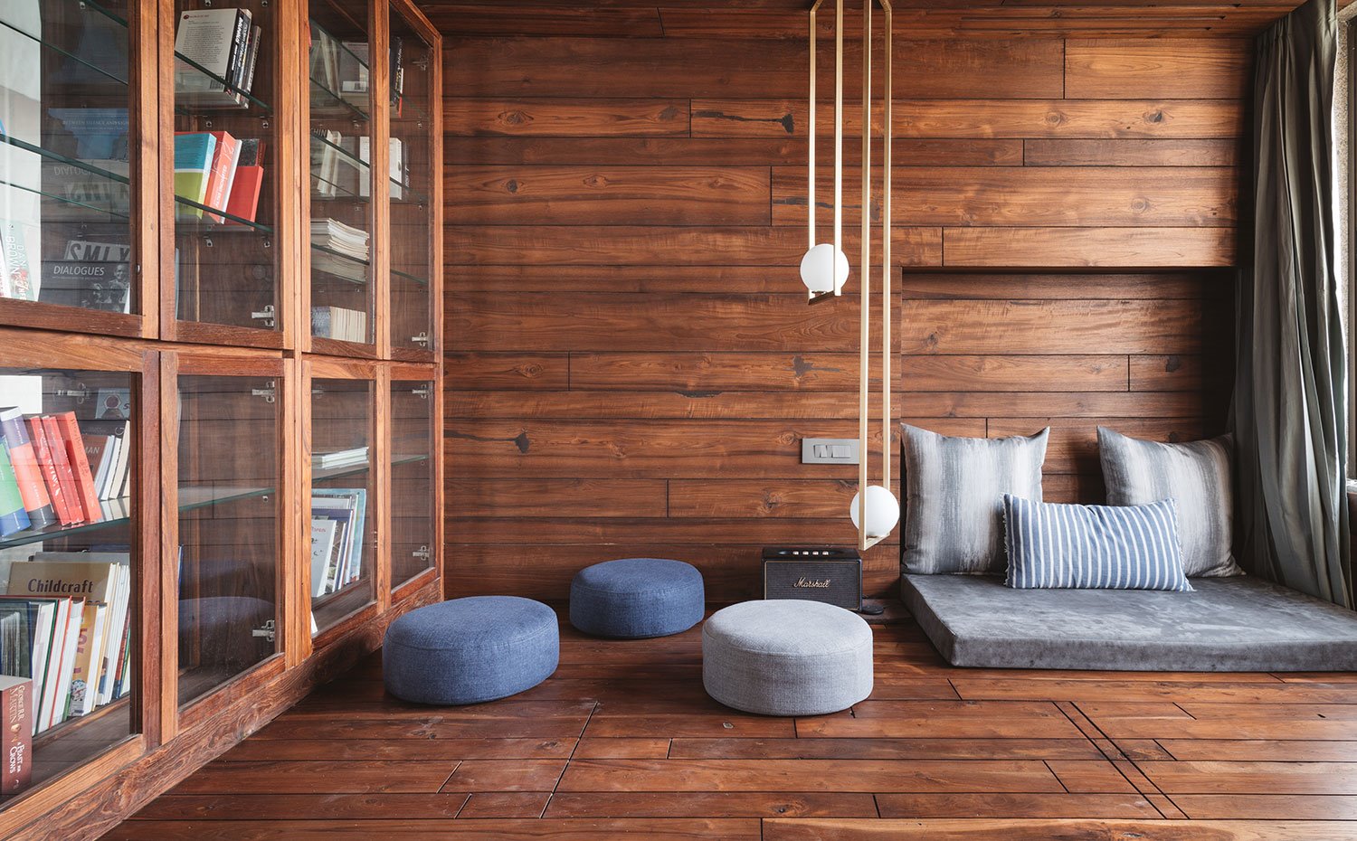 Zona de televisión con cojines y poufs, luminaria suspendida dorada y de cristal, revestimiento de madera