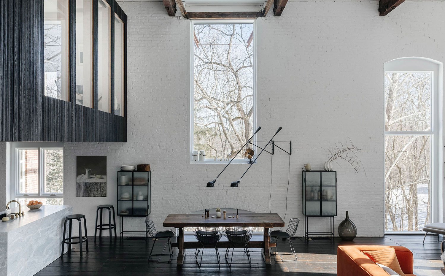 Comedor con mesa de centro de madera y sillas cromadas con cojines en negro, grandes apliques iluminan la zona 