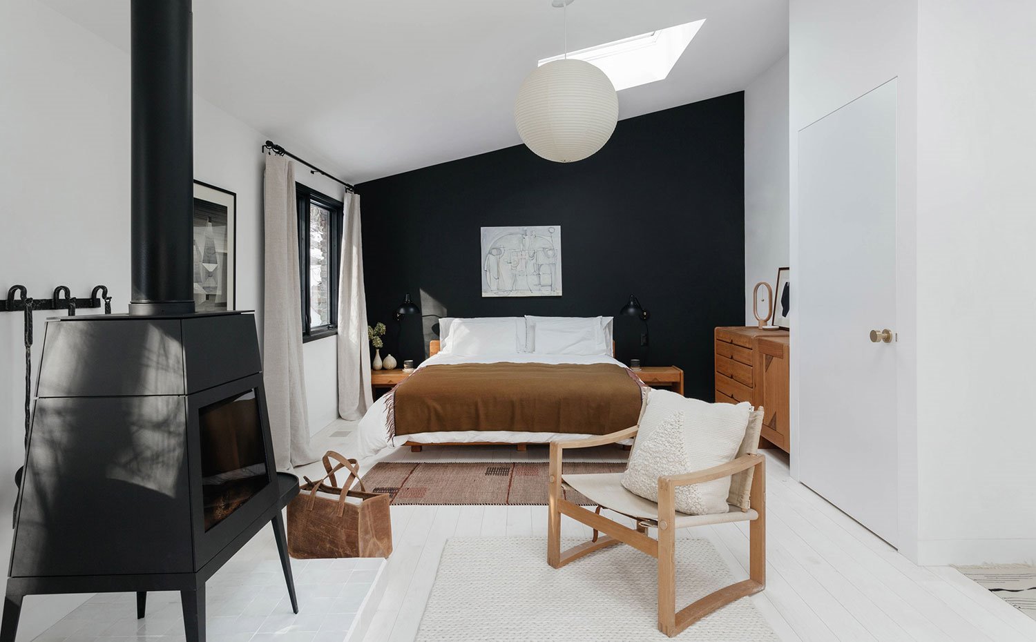 Dormitorio con chimenea en hierro fundido, pared en negro, luminaria esférica