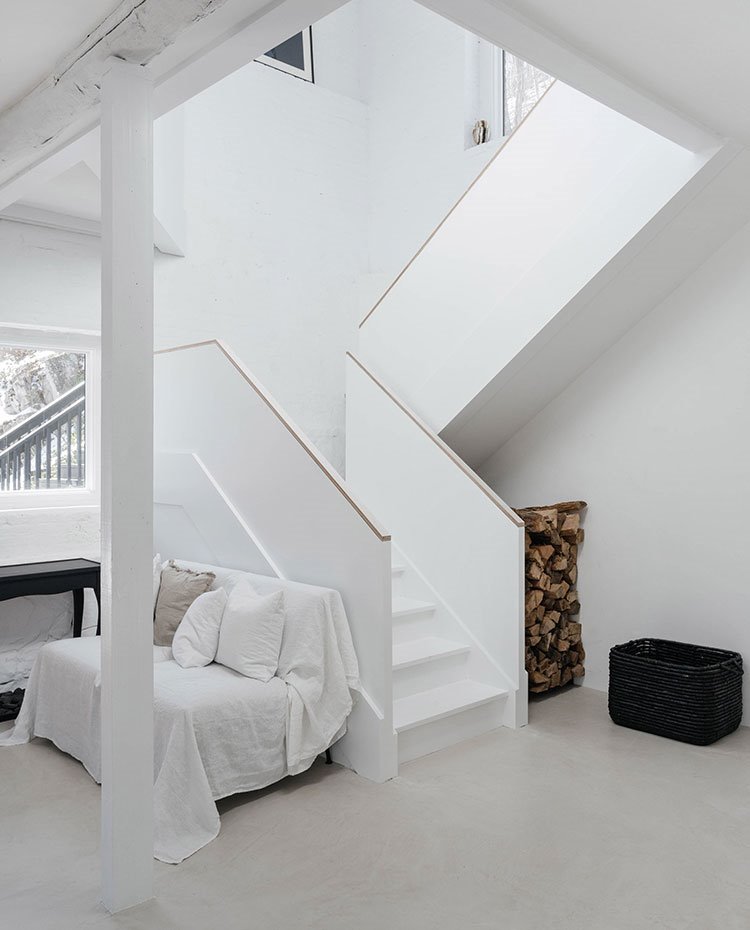 Escaleras en blanco, sofá cubierto con cojines blancos y beige, hueco escalera para madera