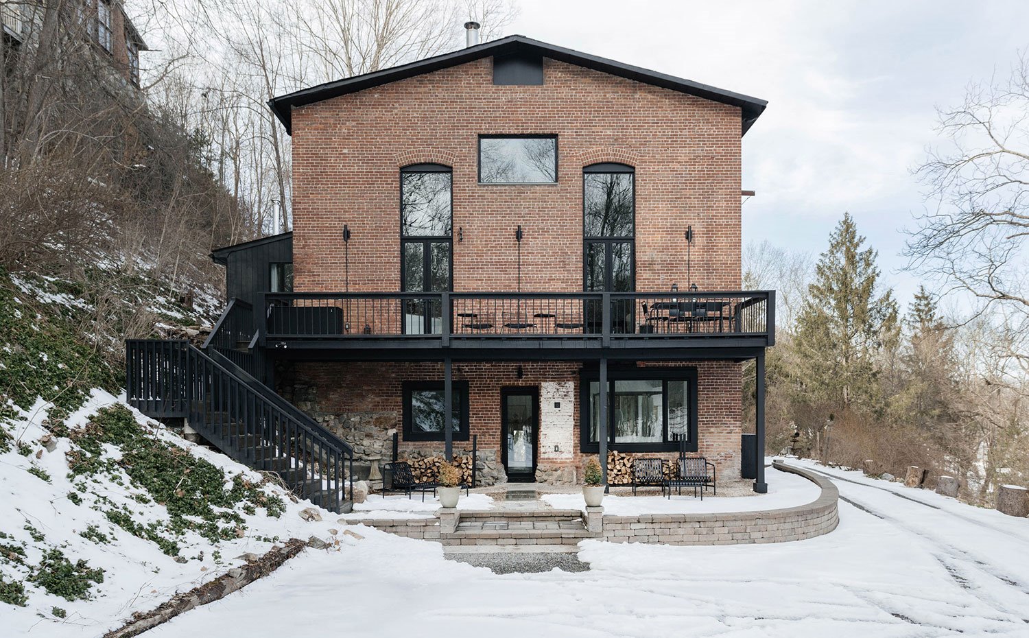 Exterior vivienda con ladrillo de obra vista, suelo de piedra y estructura de madera en negro