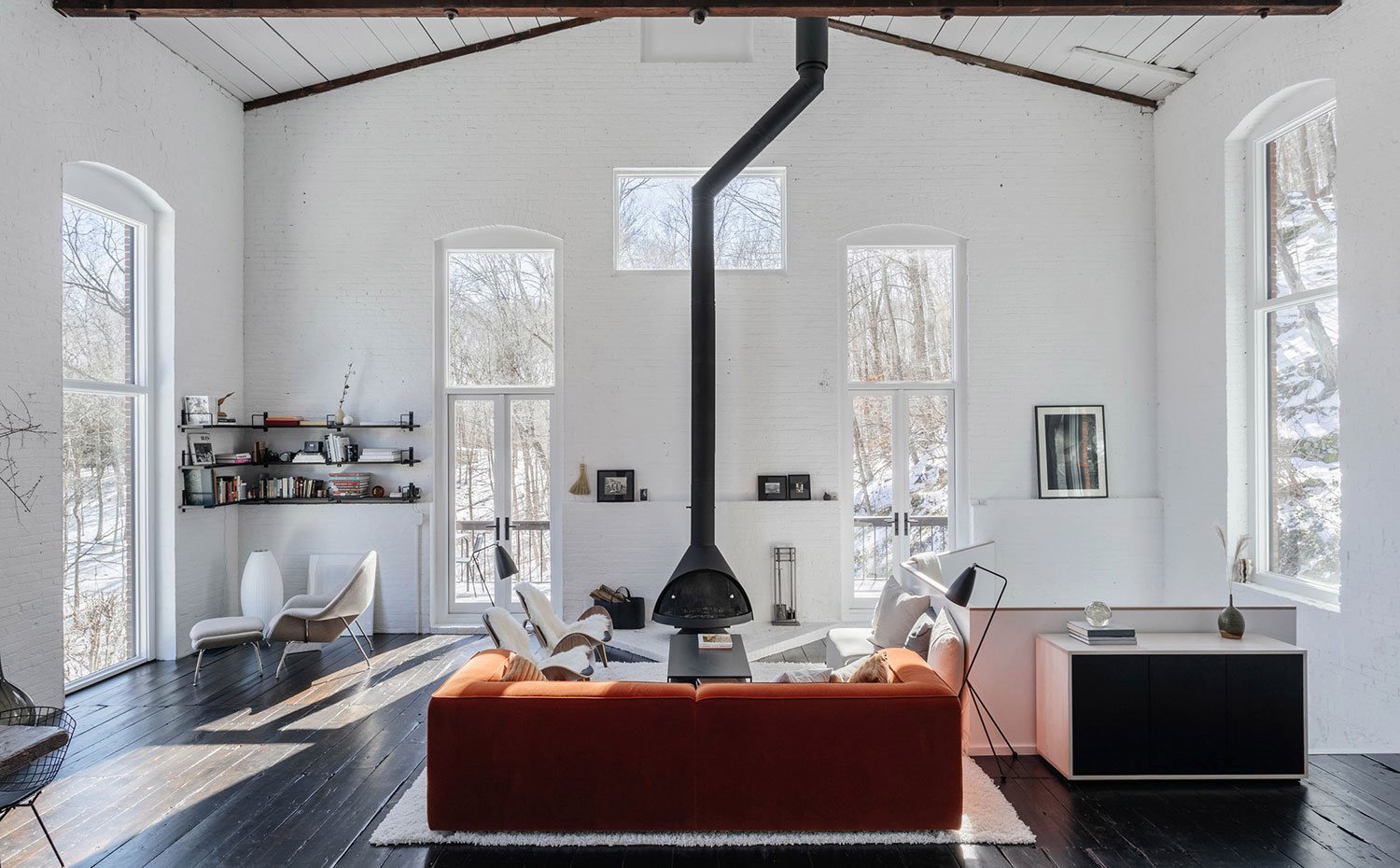 Salón con sofá en naranja frente a chimenea, con butacas en blanco y suelo de madera