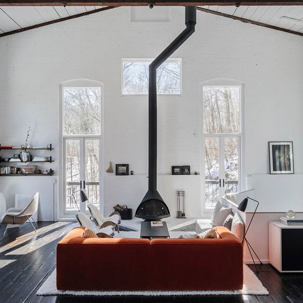 Salón con sofá en naranja frente a chimenea, con butacas en blanco y suelo de madera