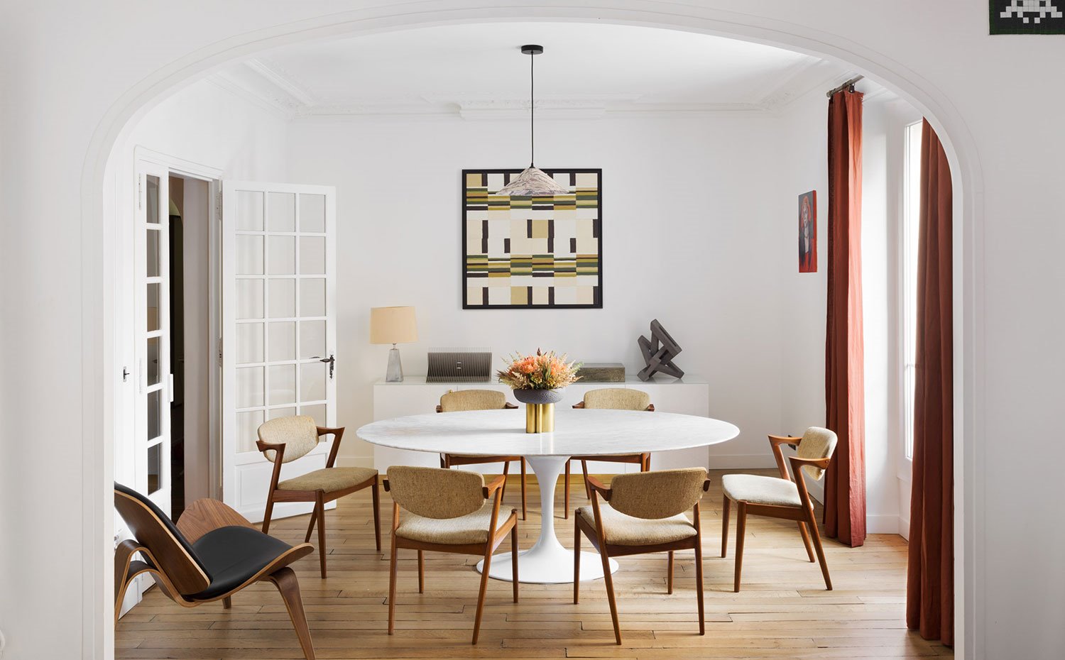 Comedor con mesa circular blanca, sillas tapizadas crudas con estructura de madera, aparador de madera