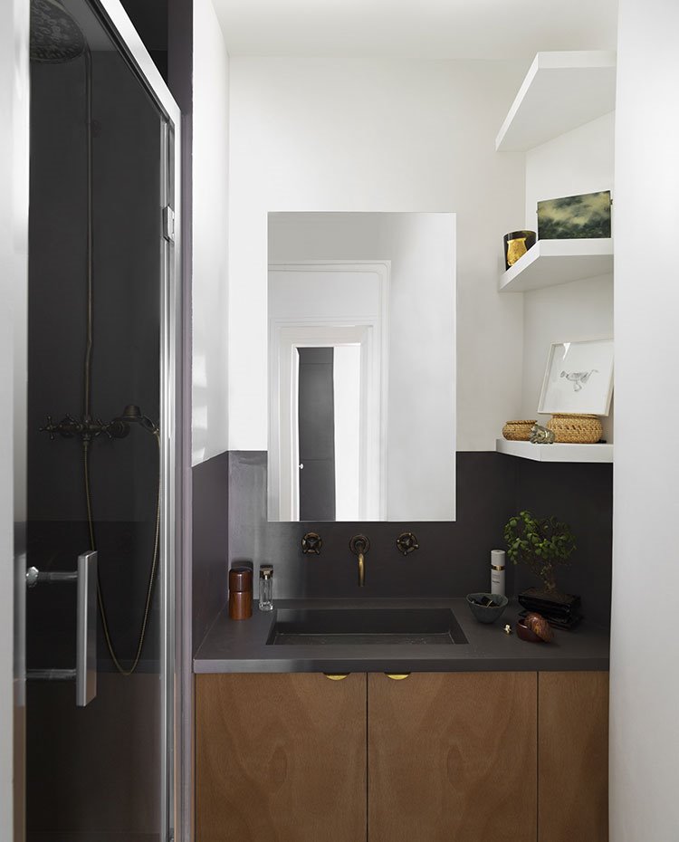 Cuarto de baño con encimera de granito negro, mobiliario en madera, baldas en blanco