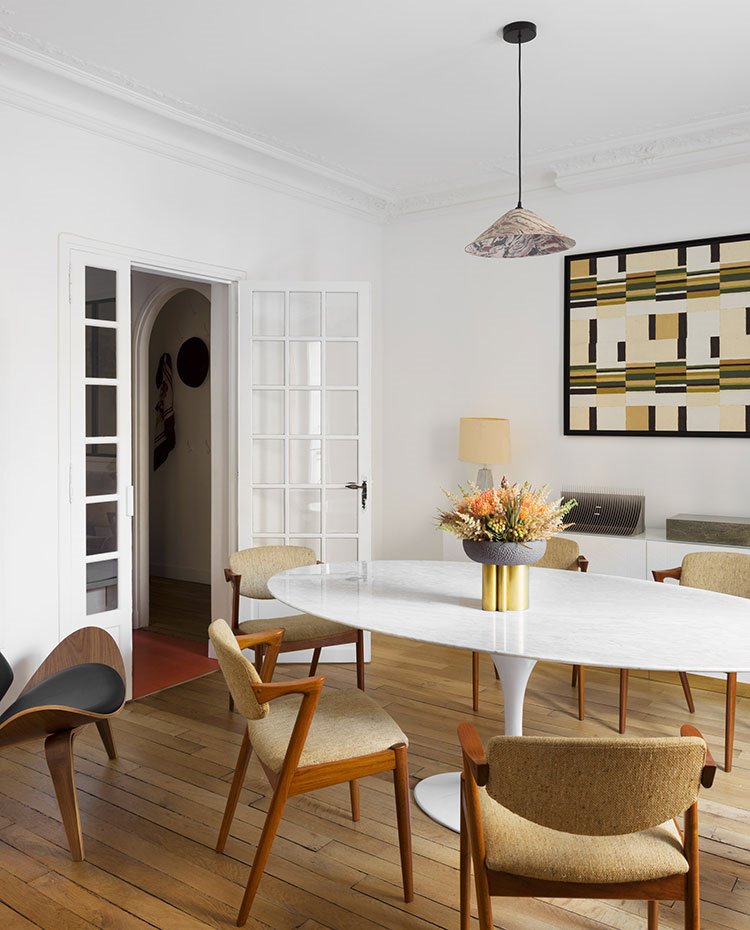Zona comedor con puerta de cristal y marcos de madera en blanco, sullas y butaca de madera, mesa de centro blanca